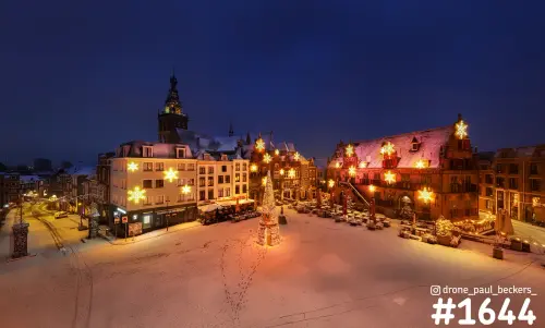 Luchtfoto van de besneeuwde Grote Markt in Nijmegen in de avond, met verlichte sneeuwvlokken en de Stevenskerk