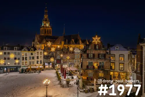 Luchtfoto van de besneeuwde Grote Markt in Nijmegen 's avonds, met verlichte sterren en de Stevenskerk erachter