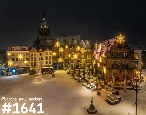 Luchtfoto van de besneeuwde Grote Markt in Nijmegen bij nacht, met Stevenskerk en lichtgevende sneeuwvlokken