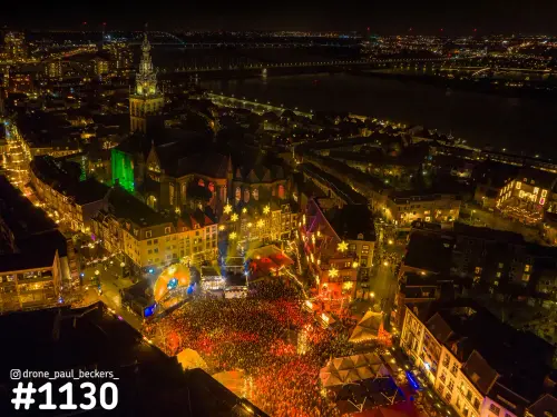 Luchtfoto van de Grote Markt in Nijmegen bij nacht, vol mensen bij een feest, met de Stevenskerk en de Waal erachter