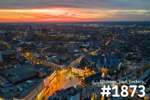Luchtfoto van de Grote Markt en Stevenskerk in het centrum van Nijmegen bij zonsondergang, met verlichte straten en oranje lucht