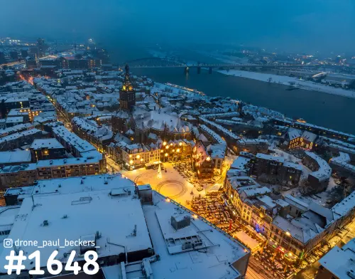 Luchtfoto van de Grote Markt en Stevenskerk in Nijmegen onder de sneeuw, met verlichte pleinen en de Waal in blauw avondlicht
