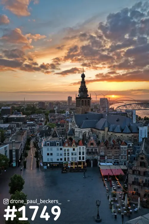 Luchtfoto van de Grote Markt en Stevenskerk in Nijmegen bij zonsondergang, met de Waal en de brug De Oversteek aan de horizon