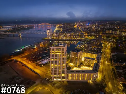Luchtfoto van verlichte hoogbouw aan de Handelskade in Nijmegen, met de Waal en de Waalbrug in de avondschemering