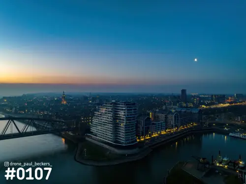 Luchtfoto van de Handelskade in Nijmegen in het blauwe uur, met verlichte Stevenskerk en de maan boven de Waal