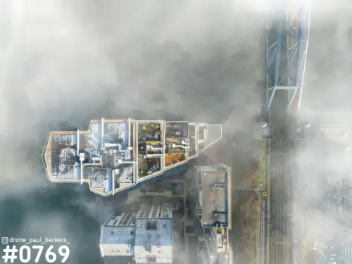 Luchtfoto recht van boven op daken aan de Handelskade in Nijmegen, met mist, een blauwe stalen brug en spoorlijn
