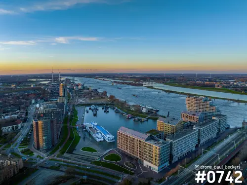 Luchtfoto van de Handelskade in Nijmegen bij zonsondergang, met de jachthaven, woongebouwen en de brede Waal op de achtergrond