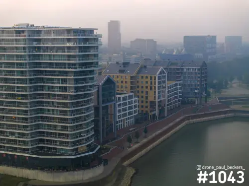 Luchtfoto van woongebouwen aan De Handelskade in Nijmegen in ochtendmist, met een gebogen appartemententoren aan de Waal