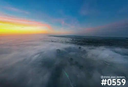 Luchtfoto van de Handelskade in Nijmegen met gebouwen die boven een dik mistdek uitsteken onder een oranje en blauwe lucht