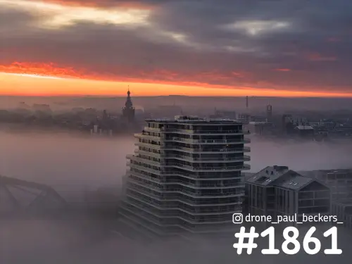 Luchtfoto van een flatgebouw aan de Handelskade in Nijmegen in mist, met de Stevenskerk en een oranje ochtendhemel