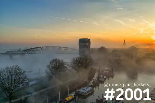 Luchtfoto van de Handelskade in Nijmegen in ochtendmist, met woonboten, stalen brug en de torenspits van de Stevenskerk
