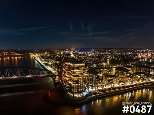 Luchtfoto van de Handelskade in Nijmegen bij nacht, met verlichte hoogbouw aan de Waal en de Waalbrug links