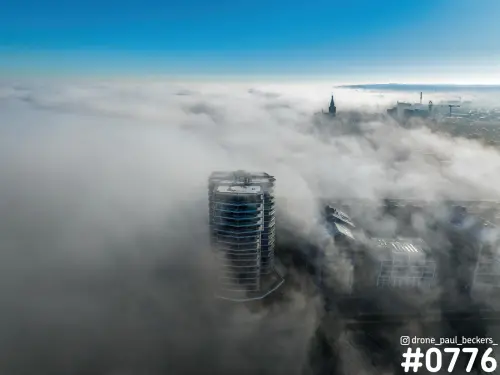 Luchtfoto van een hoogbouwtoren aan de Handelskade in Nijmegen die boven de mist uitsteekt, met de Stevenskerk in de verte