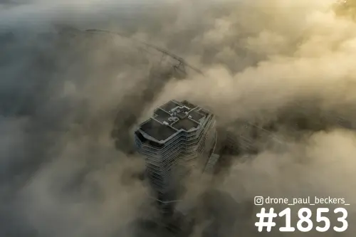 Luchtfoto van een torengebouw aan de Handelskade in Nijmegen dat boven dichte mist uitsteekt, met een brugboog erachter