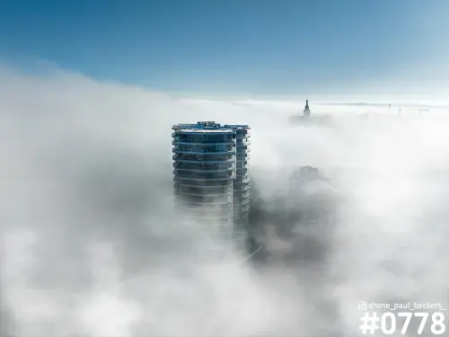 Luchtfoto van de woontoren aan de Handelskade in Nijmegen die boven een dik mistdek uitsteekt, met de Stevenskerk op de achtergrond