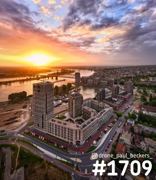 Luchtfoto van de Handelskade in Nijmegen met hoogbouw aan de Waal, onder een kleurrijke lucht met laagstaande zon