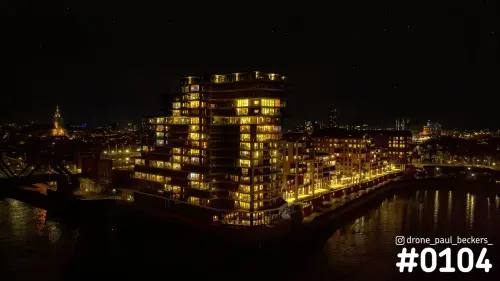 Luchtfoto van verlichte appartementengebouwen aan de Handelskade in Nijmegen bij nacht, met reflecties in de Waal