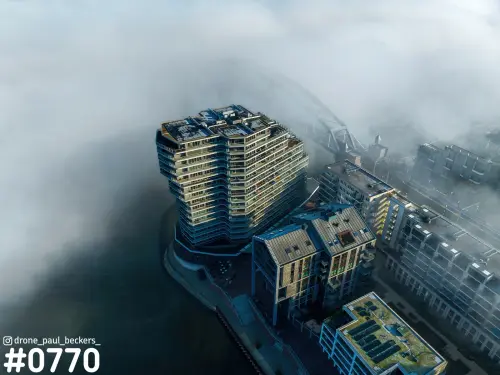 Luchtfoto van de Handelskade in Nijmegen: woontoren en appartementen aan de Waal omringd door dikke mist