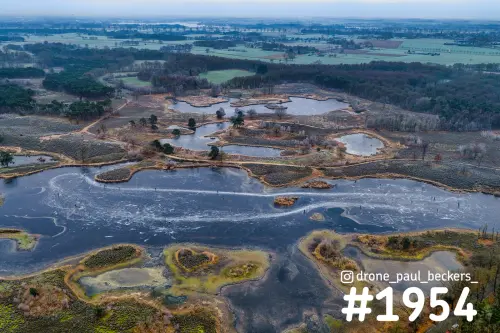 Luchtfoto van de Hatertse Vennen met een ijsvlakte, heide-eilandjes en kleine vennen in grijs winterlicht