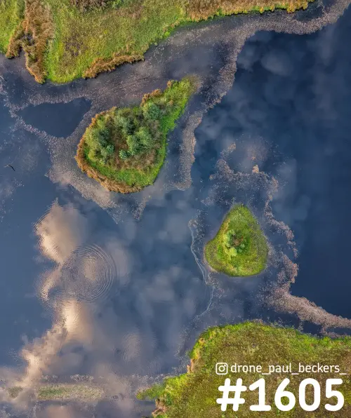 Luchtfoto van twee eilandjes in de Hatertse Vennen, Nijmegen, met wolken weerspiegeld in het water en rimpelcirkels
