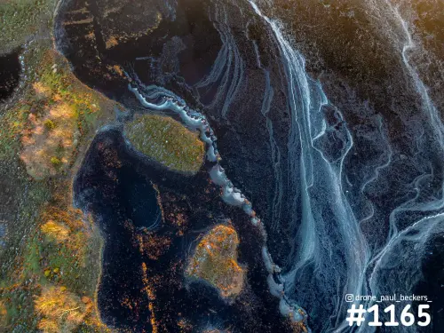 Luchtfoto van de Hatertse Vennen bij Nijmegen: witte ijspatronen op donker water naast oranje en groene begroeiing