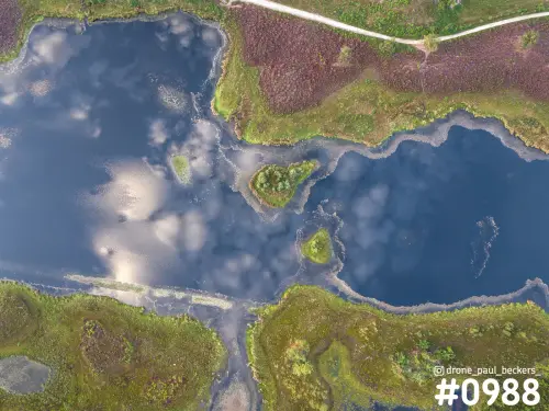 Luchtfoto recht van boven op de Hatertse Vennen bij Nijmegen, met kleine eilandjes in donker water en paarse heide langs de oever