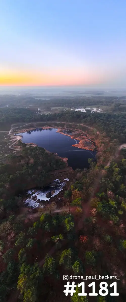 Luchtfoto van de Hatertse Vennen bij Nijmegen in de schemering, met een donker ven, dennenbos en ijsresten op het water