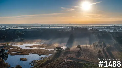 Luchtfoto van de Hatertse Vennen bij zonsopkomst, met zonnestralen door de mist tussen heide, vennen en bomen