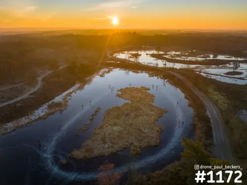 Luchtfoto van schaatsers op het ijs van de Hatertse Vennen bij Nijmegen, met laagstaande zon en een graseiland