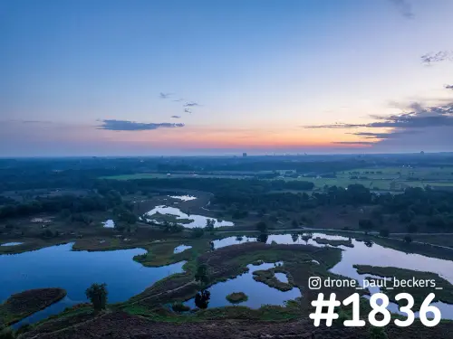 Luchtfoto van de Hatertse Vennen bij Nijmegen na zonsondergang, met kleine vennen in het heidelandschap en een oranje gloed aan de horizon