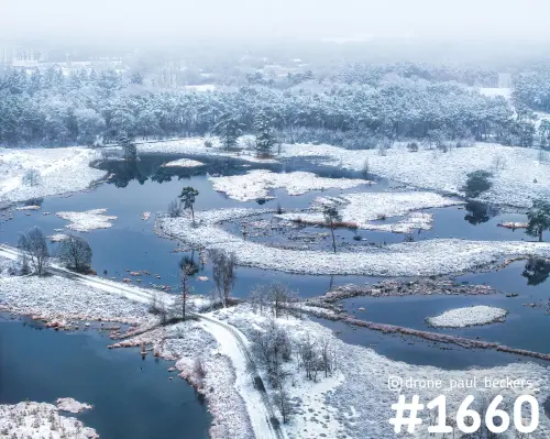 Luchtfoto van de Hatertse Vennen bij Nijmegen in de sneeuw, met open water, besneeuwde oevers en dennenbos in de mist