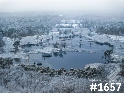 Luchtfoto van de Hatertse Vennen bij Nijmegen in de sneeuw, met een stil ven omringd door berijpte bomen en mist