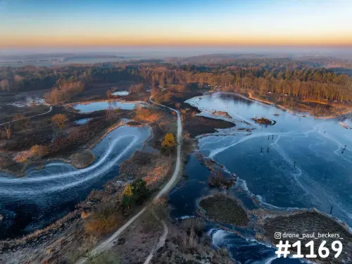 Luchtfoto van de Hatertse Vennen in de winter met bevroren vennen, een zandpad door de heide en een oranje horizon