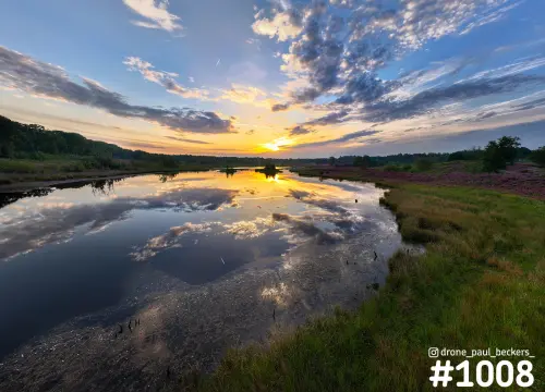 Luchtfoto van de Hatertse Vennen bij zonsondergang, met wolken weerspiegeld in het water en bloeiende heide op de oever