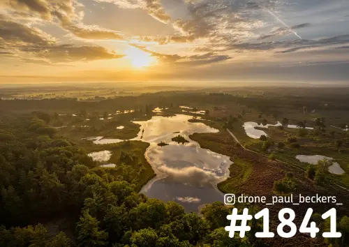 Luchtfoto van de Hatertse Vennen bij zonsopkomst, met wolken weerspiegeld in een ven tussen bos en heide