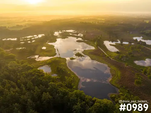 Luchtfoto van de Hatertse Vennen bij zonsopkomst, met wolken weerspiegeld in de vennen en heide tussen het bos