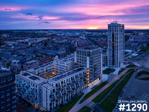 Luchtfoto van appartementen met zonnepanelen en een hoogbouwtoren in het Havenkwartier onder een roze avondhemel