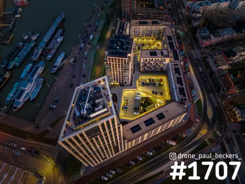 Luchtfoto van woontorens in het Havenkwartier in Nijmegen in de avondschemering, met verlichte daktuinen en woonboten in de haven