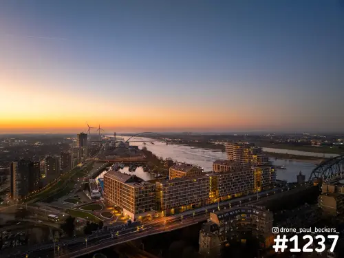 Luchtfoto van de Handelskade en het Havenkwartier in Nijmegen bij schemering, met de Waal en een oranje gloed aan de horizon