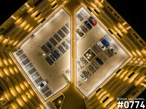 Luchtfoto recht van boven op een verlicht parkeerhof in het Havenkwartier in Nijmegen, 's nachts, met auto's tussen gele gevels