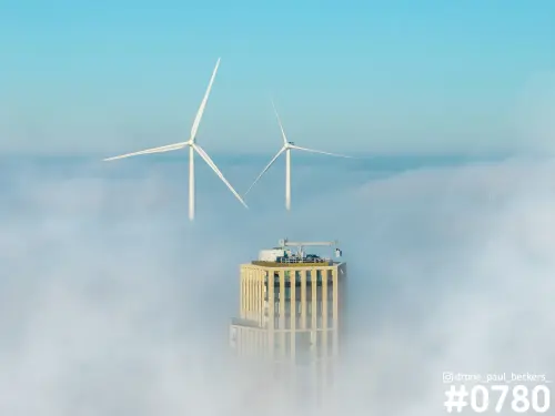 Luchtfoto van een hoogbouwtoren in het Havenkwartier in Nijmegen, met twee windturbines boven een dik mistdek