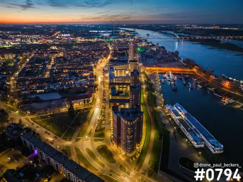 Luchtfoto van het Havenkwartier in Nijmegen in de avondschemering, met verlichte woontorens, de Waal en De Oversteek in de verte