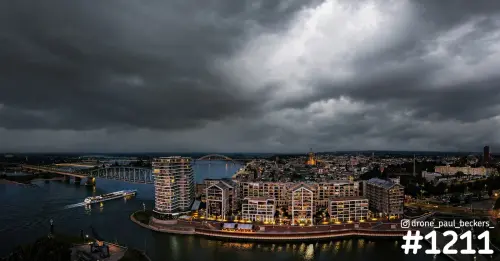 Luchtfoto van het Havenkwartier in Nijmegen aan de Waal in de avond, met donkere wolken boven het centrum en een rivierschip
