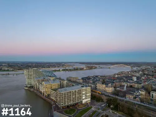 Luchtfoto van appartementen aan de Waal in het Havenkwartier van Nijmegen, met de Waalbrug in de verte bij schemering