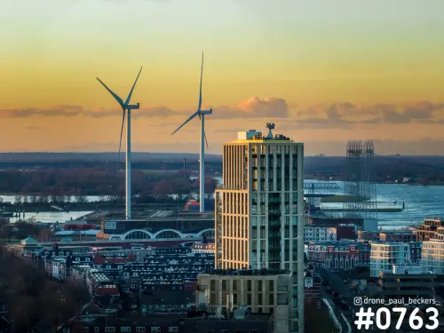 Luchtfoto van een woontoren in het Havenkwartier in Nijmegen bij zonsondergang, met windturbines en de Waal op de achtergrond