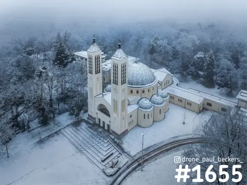 Luchtfoto van de kerk met twee torens en koepel van de Heilig Land Stichting bij Nijmegen, onder sneeuw en mist