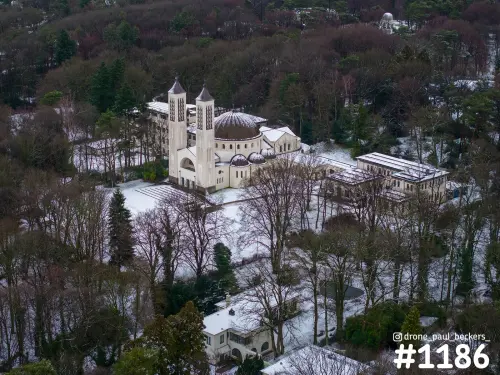 Luchtfoto van de koepelkerk met twee torens in het Heilig Land Stichting bij Nijmegen, met sneeuw tussen de kale bomen