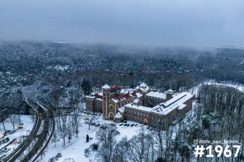 Luchtfoto van de Heilig Landstichting bij Nijmegen in de sneeuw: baksteencomplex met toren in een mistig bos