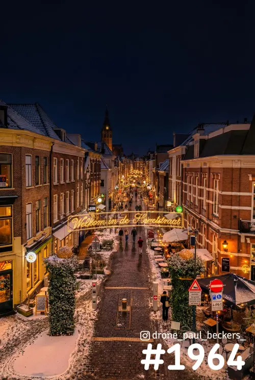 Luchtfoto van de besneeuwde Hemelstraat in Nijmegen in de avond, met verlicht welkomstbord en de Stevenskerktoren