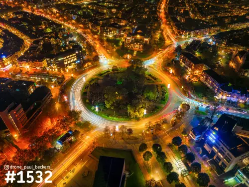 Luchtfoto van het Keizer Karel Plein in Nijmegen 's avonds, met lichtsporen van verkeer rond de rotonde met bomen